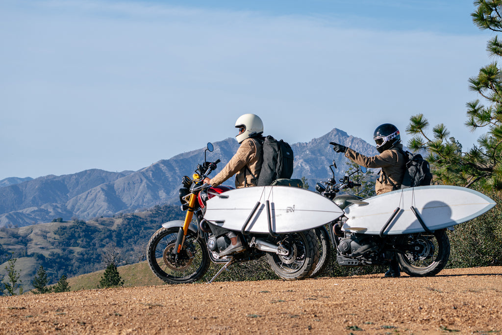 Photo of two motorcyclists stopped on a ridge, with surfboards attached to the side of their motorcycles, looking off into the distance and talking via their Cardo Communication Systems on their helmets